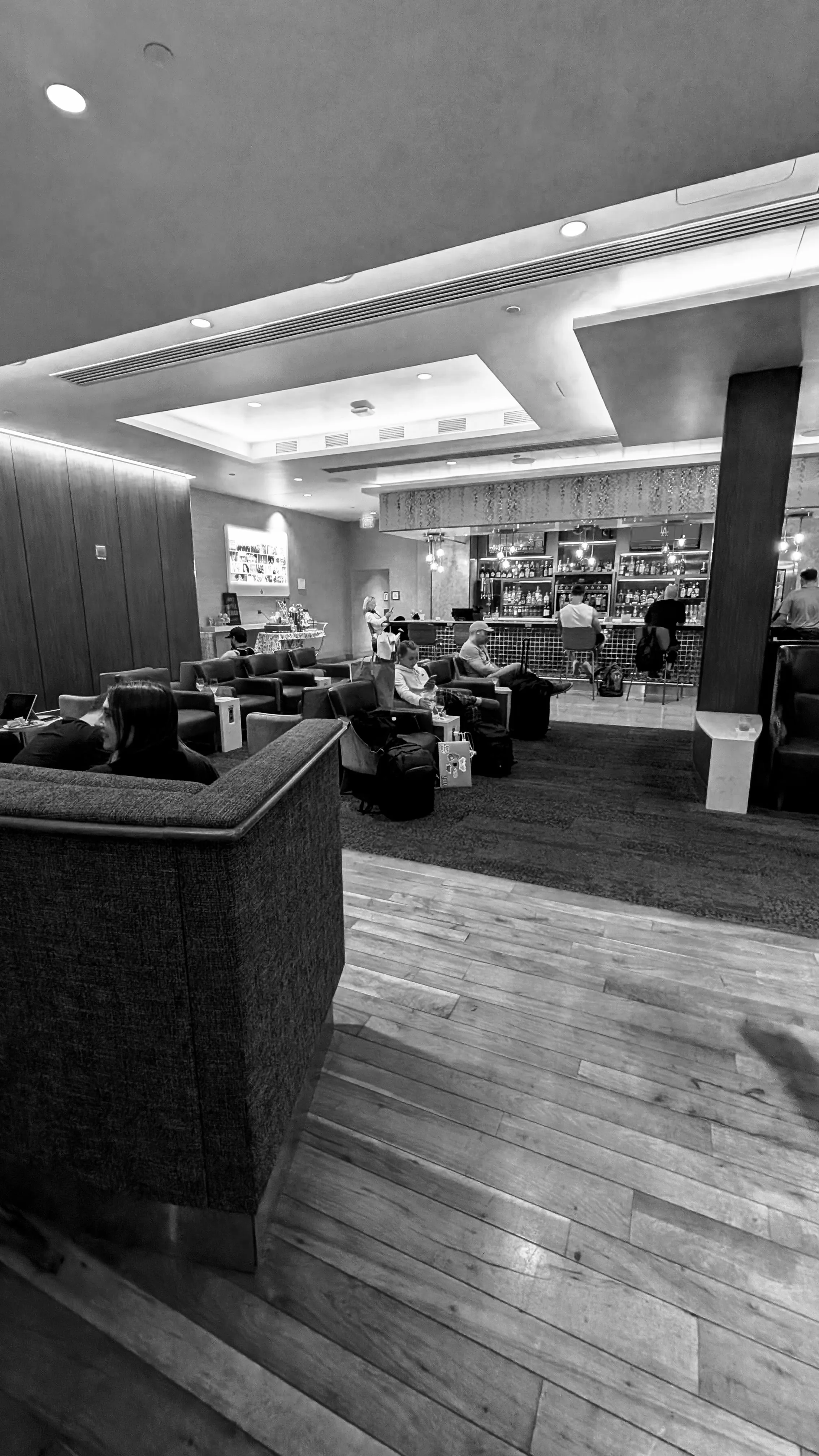 A finished airline club in Detroit, with travelers seated near the bar.