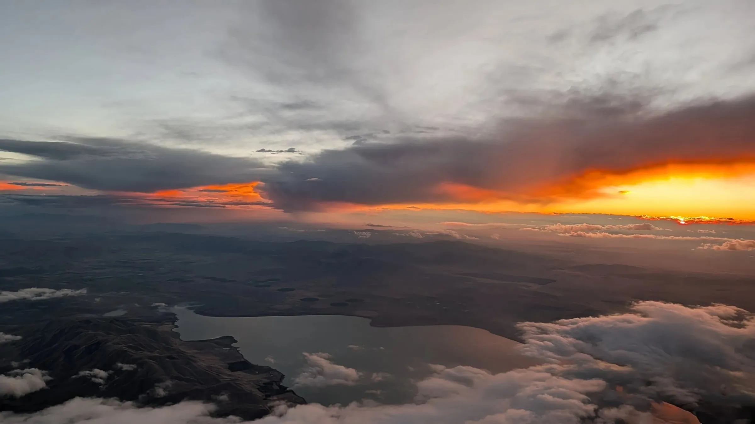 The sun going down over water and broken cloud, seen from the window seat.