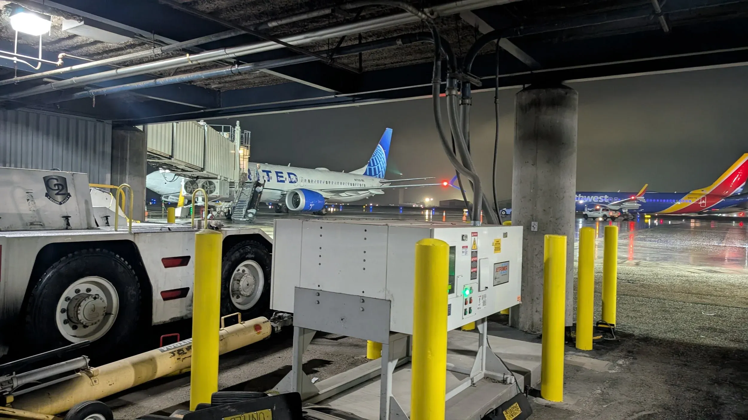 An aircraft at a gate seen from ramp level, ground equipment in the foreground.